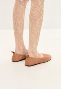 Ballet flats de cuero color tostado con punta redondeada y suave fruncido en el talón, combinados con medias de red beige con patrones florales.