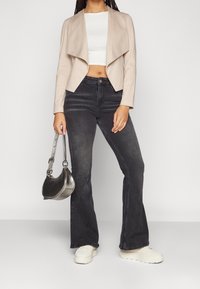 Bežová kabátová bunda, bílý crop top, černé zvonové džíny, metalická kabelka a bílé platformové tenisky. Hladké textury a moderní design.