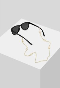 Occhiali da sole neri con lenti scure, sostenuti da una catena dorata con dettagli ovali. La catena è leggera e decorativa.