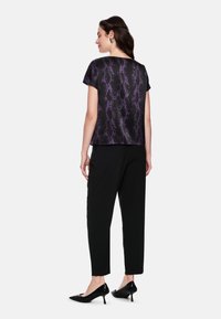 Black top with a purple snake print pattern, short sleeves, paired with black tapered trousers and black pointed heels.