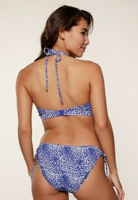 Set bikini in stampa animale blu e bianco. Presenta un top con lacci posteriori e dettagli in metallo e slip bikini con lacci laterali. Texture liscia, design a vita media.