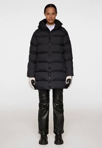 Svart vadderad jacka med dragkedja framtill och huva. Har ett quiltat mönster och ribbade muddar. Bärs med svarta skinnbyxor och handskar.