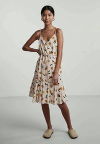 Robe imprimée florale en beige clair avec des accents orange et vert, dotée d'un décolleté en V, de bretelles ajustables et d'une jupe évasée.