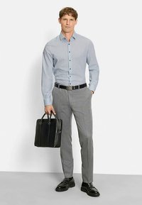 Light blue checkered shirt, gray plaid trousers, black belt and shoes, holding a black leather bag with white accents. Casual business attire.