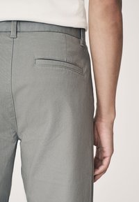 Pantaloni grigi con una texture liscia, dotati di una tasca posteriore con patta e una vita aderente. Il tessuto è leggero e casual.