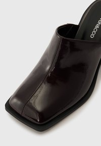 Glanzend donkerburgundy open teen mule met een vierkante neus en slank design. Voorzien van een zwarte zool en minimaal stiksel.