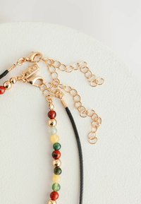 Collier en perles avec cuir noir et pierres multicolores (rouge, vert, jaune) avec quincaillerie dorée et extension en chaîne.