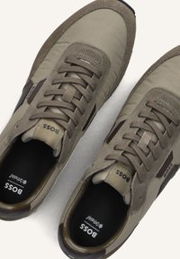 Beige sport schoenen met een combinatie van textiel en suede materialen. Vetersluiting met donkerbruine accenten en logo aan de zijkanten.