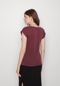 Blusa curta marrom com mangas curtas, feita de um tecido macio, com um decote redondo e mangas dobradas. Textura suave, design ligeiramente ajustado.