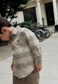 Camicia a quadri beige e marrone, con una texture morbida, maniche lunghe e un piccolo logo a forma di orso sul petto.