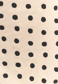 Beige stof met een herhaald patroon van stevige zwarte stippen, die iets in grootte variëren. De textuur lijkt zacht en licht.