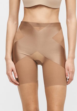 Nude tvarovacie šortky s vysokým pásom a cieľovými kompresnými panelmi pokrývajúcimi bruško, boky a stehná na stojacej modelke.