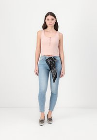 Világos rózsaszín bordázott ujjatlan felső gombos részlettel, világoskék slim fit farmernadrággal párosítva. Fekete mintás bandana megkötve a derékon. Texturált szürke cipők.
