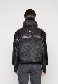 Czarna kurtka puchowa z skórzanymi rękawami, z wysokim kołnierzem, subtelnym geometrycznym wzorem i logo na plecach. Teksturowane materiały i zamki błyskawiczne.