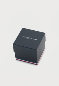 Scatola per orologio Tommy Hilfiger, forma quadrata, finitura opaca blu navy, logo sulla parte superiore, strisce di accento bianche e rosse alla base.