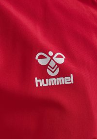 Rød tekstil med et hvidt logo, der viser en stiliseret bi og teksten "hummel." Stoffet ser glat ud med en let glans.