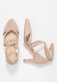 Scarpe con tacco alto in suede nudo con punta affusolata, design a strap incrociata e tacco sottile. Texture liscia con una soletta leggermente lucida.