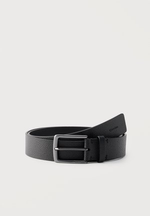 Cintura in pelle nera con texture e fibbia rettangolare argentata opaca, parzialmente arrotolata su sfondo bianco.