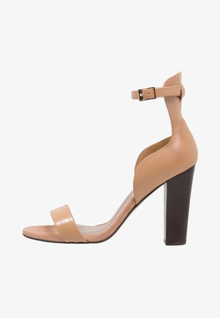 Sandale à talon haut en cuir camel avec une large bride sur le pied, une bride à la cheville avec une boucle, et un talon bloc solide. Texture lisse et design minimaliste.