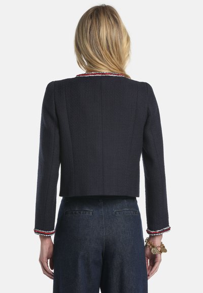 Veste courte bleu marine en tissu texturé, manches longueur bracelet, avec un galon multicolore le long du col et des poignets.