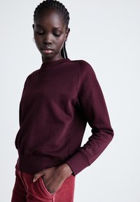 Sweat-shirt à col rond bordeaux en mélange de coton avec des poignets et un ourlet côtelés. Design minimaliste avec broderie sur la manche gauche.