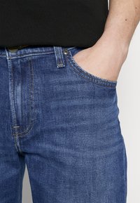 Jeans in denim blu medio, con una vestibilità classica, design a cinque tasche, leggera usura e cuciture dorate a contrasto.