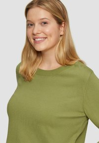 Groene gebreide trui met een ronde halslijn en ribbelboord. De stof lijkt zacht en glad van textuur. Geen zichtbare patronen of accenten.