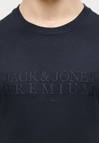 Μπλε πουκάμισο ναυτικού με ανάγλυφο κεντημένο κείμενο "JACK & JONES PREMIUM" και "EST. 1990" στο στήθος.