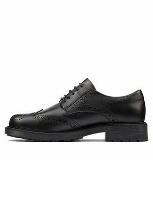 Chaussure brogue en cuir noir avec perforations en forme d’aile, fermeture à lacets et semelle épaisse crantée, vue de profil sur fond blanc.