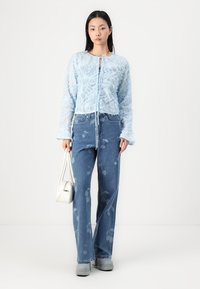 Light blue lace top with long sleeves and tie closure; high-waisted jeans with floral patterns; white handbag; gray platform shoes.