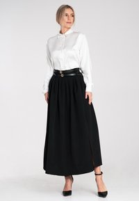 Weiße Satinbluse mit Kragen, kombiniert mit einem schwarzen plissierten Maxirock mit seitlichen Schlitzen und einem schwarzen Gürtel mit goldenen Akzenten.