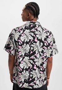 Camisa de manga corta en negro, blanco y patrón floral rosa. Presenta un ajuste relajado, cuello con puntas y tela ligera.