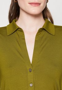 Oliven grøn, kortærmet skjorte med knaplukning og krave, lavet af et glat, tekstureret stof.