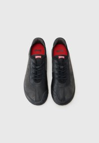 Baskets noires avec un mélange de cuir et de tissu, design à lacets, surfaces texturées, branding Camper rouge et blanc, et semelles en caoutchouc.