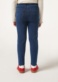 Jeans de mezclilla azul oscuro con un ajuste ceñido, que cuentan con una cinturilla elástica y dos bolsillos traseros. Combinados con calzado rojo para crear contraste.