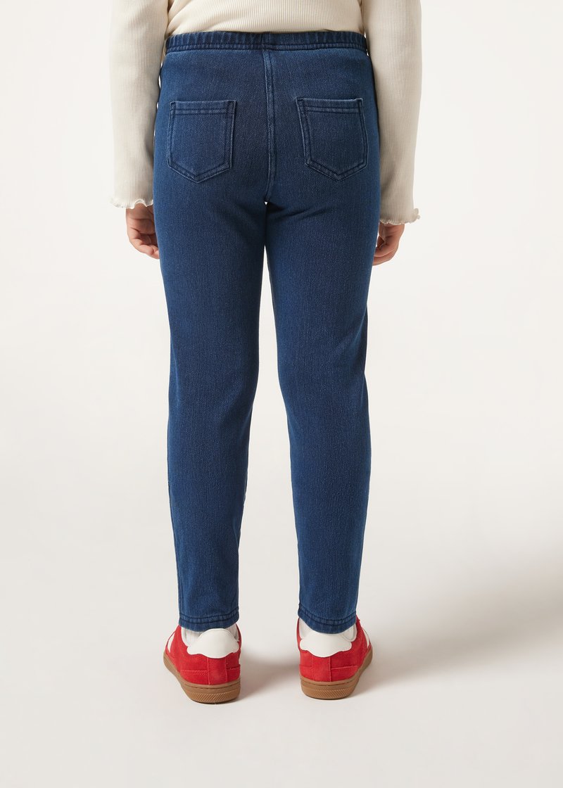 Jeans de mezclilla azul oscuro con un ajuste ceñido, que cuentan con una cinturilla elástica y dos bolsillos traseros. Combinados con calzado rojo para crear contraste.