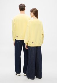 Ανοιχτό κίτρινα φούτερ με άνετη εφαρμογή, με ραβδωτά μανσέτες και τελείωμα, συνδυασμένα με ευρύχωρα τζιν παντελόνια σε σκούρο χρώμα. Ορατές ετικέτες με λογότυπο.
