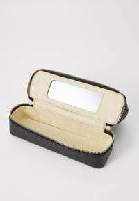Custodia in pelle nera con una texture liscia, zip dorata, interno beige morbido e una toppa a specchio rettangolare sul coperchio.