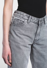 Graue Jeans aus Denim mit hoher Taille und geradem Schnitt. Verfügt über fünf Taschen, Metallbeschläge und eine strukturierte Stoffoberfläche.
