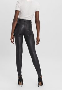 Zwarte high-waisted leggings met een glanzende, nep-lederen textuur. Bevat achterzakken en stiksels details. Gemaakt met een aansluitend wit top.