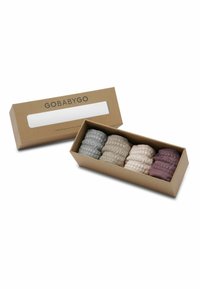 Quatre chaussettes bébé texturées en gris, beige, crème et bordeaux, disposées dans une boîte en carton marron ouverte portant l'étiquette GOBABYGO.