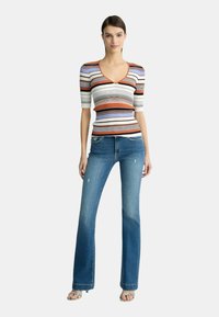 Stribet striktrøje i orange, hvid, lavendel og sort med v-hals; parret med lyseblå, flagrende denimjeans med slidte detaljer.
