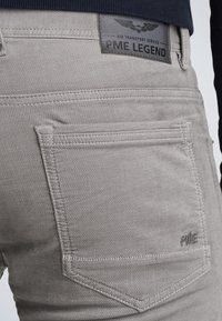 Pantalones de mezclilla gris con una textura suave, dos bolsillos traseros y una etiqueta de cuero con "PME Legend" y un emblema de alas.