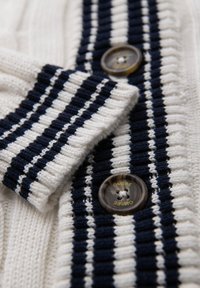 Cardigan a righe realizzato in tessuto a maglia blu navy e bianco. Dettagli notevoli includono un bottone trasparente con la scritta "OMBRE" incisa e una texture a coste.