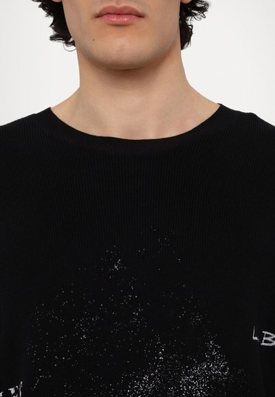 Pull en tricot côtelé noir avec un col rond et un design éclaboussé blanc avec des accents de texte sur le devant.
