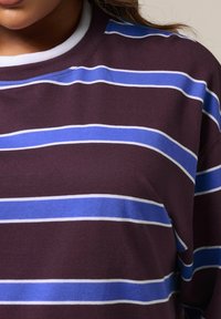 Bordowy sweatshirt z poziomymi paskami w jasnoniebieskim i białym kolorze. Ma okrągły dekolt i miękką, strukturalną tkaninę.