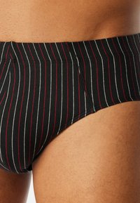 Culotte rayée noir et blanc avec des accents rouges ; fabriquée à partir d'un tissu extensible ; design ajusté ; coutures visibles le long de la taille.