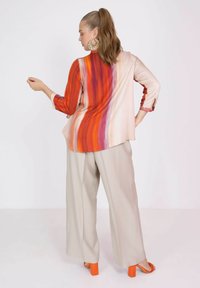 Blouse met lange mouwen in rood, oranje en beige gradient strepen; gecombineerd met crèmekleurige wijde broek; oranje block-heeled sandalen.