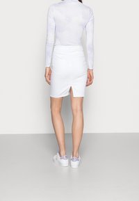 Witte denim kokerrok met een achterste splitdetail, gecombineerd met een lichtpaarse top met lange mouwen en een wolkenpatroon. Witte sneakers.