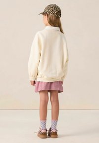 Sweatshirt crème, jupe en velours côtelé rose, casquette à imprimé léopard, chaussettes à motifs et baskets brunes. Coupe douce et décontractée avec des accents côtelés.